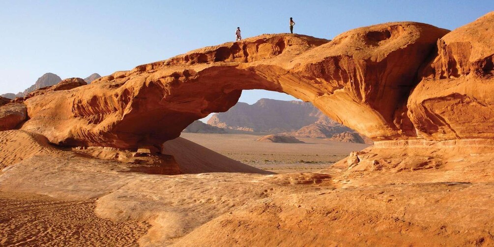 A natural rock arch formation with two people standing on top. 4