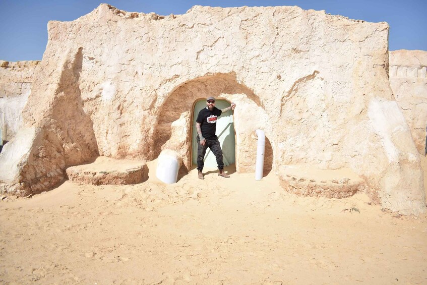 A person standing in front of a mud-brick structure with an archway. 1