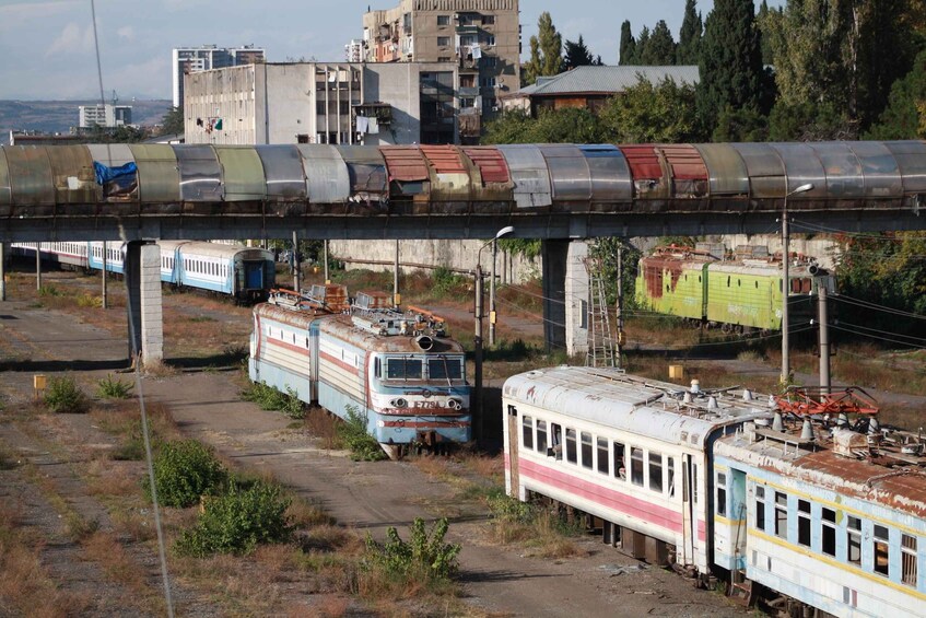 A train station with several derailed trains and a bridge overhead. 4