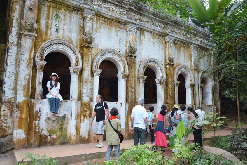 A group of people visiting an ancient, weathered building with multiple arches and columns, surrounded by lush greenery. 2