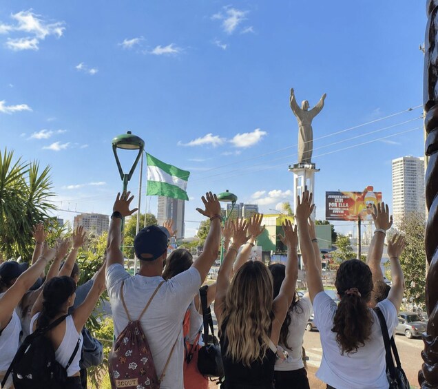 A group of people raising their hands in celebration, a statue, and a flag. 2