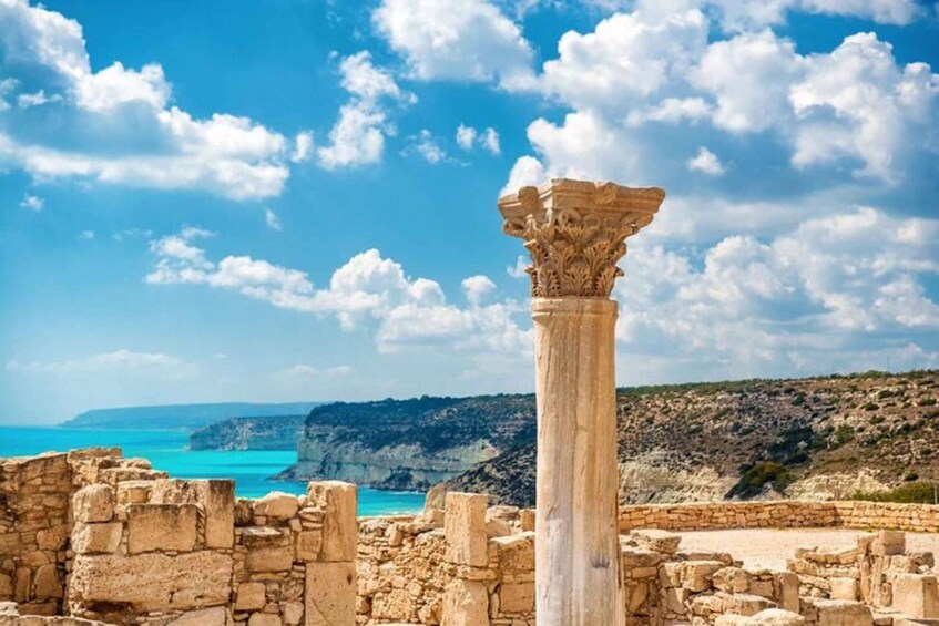 Ancient ruins with a column and stone walls, overlooking a coastal landscape with cliffs and turquoise sea. 2
