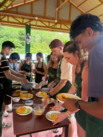 A group of people preparing food outdoors, wearing aprons, with a table full of dishes and ingredients. 5