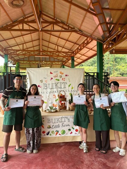 A group of people standing under a covered area with a banner that reads 'BUKIT'S Little Farm Cooking Class.' 3