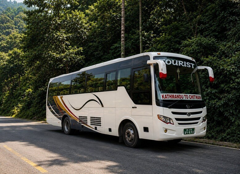 A white bus with 'TOURIST' and 'KATHMANDU TO CHITWAN' on the front, parked on a road with dense green foliage in the background. 2