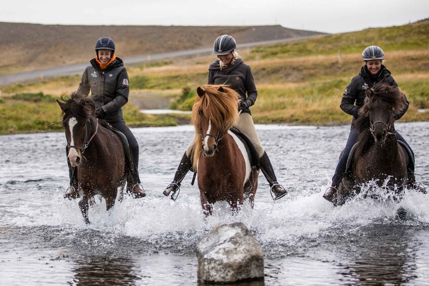Three people riding horses through a shallow body of water. 5