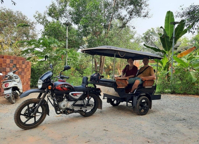 A man and woman riding a three-wheeled vehicle with a motorcycle parked nearby. 1