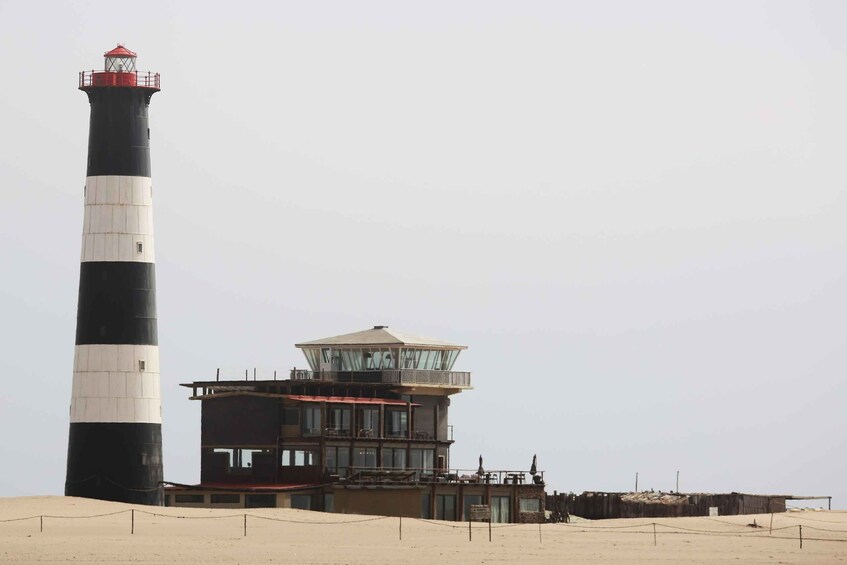 A lighthouse with a control tower, a sandy beach, and a clear sky. 1