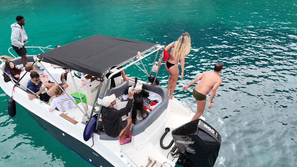 A boat with people on board, some standing and some seated, with a clear blue sea in the background. 2