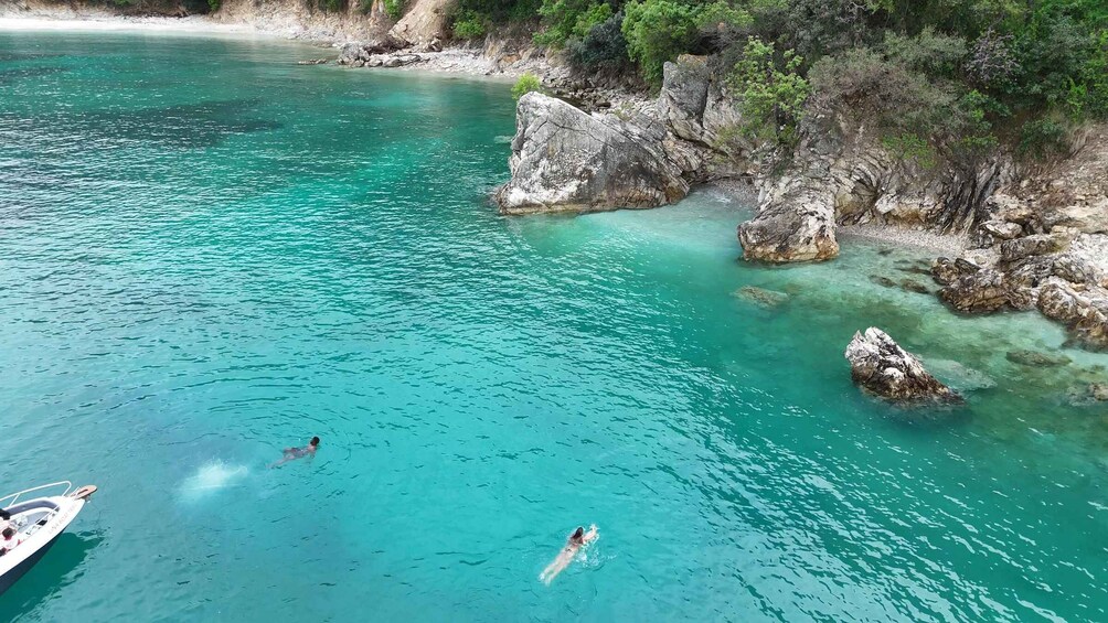 A swimmer in clear turquoise water, rocky coastline, and a boat in the foreground. 3