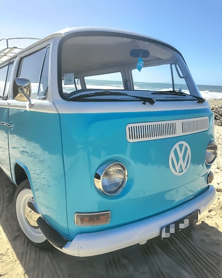 A blue Volkswagen camper van parked on a sandy beach with the ocean in the background. 1