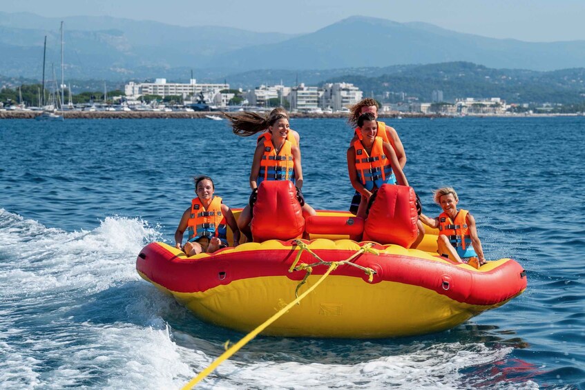 A group of people on a yellow and red inflatable raft with life jackets, moving through the water. 2
