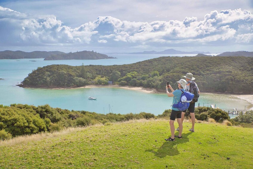 A coastal landscape with a clear sky, a small boat on the water, and two people taking a photo. 3