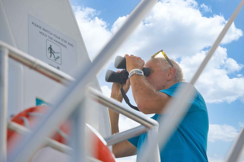 A person using binoculars, wearing a blue shirt and a wristwatch, with a sign about handrail usage in the background. 4