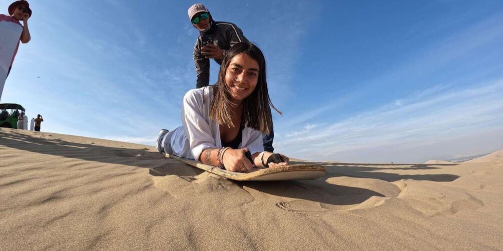 A person lying on a sand dune with a camera in the background. 3
