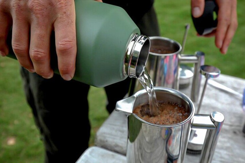 A person pouring a liquid from a green bottle into a metal container on a table. 2