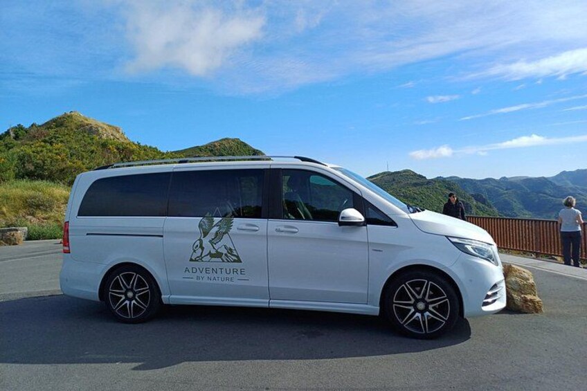 A white van with 'Adventure by Nature' written on the side parked on a road with mountains in the background. 2