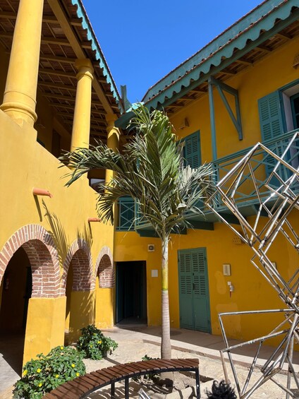 A courtyard with yellow walls, a palm tree, and a metal staircase. 1