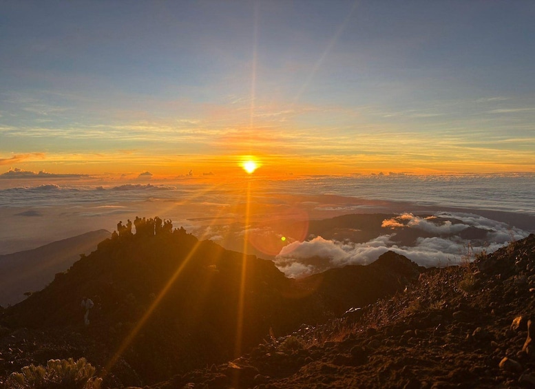 Een zonsopgang boven een bergachtig landschap met wolken eronder. 3