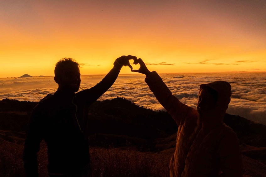 Twee personen vormen een hart met hun handen voor een zonsondergang. 1