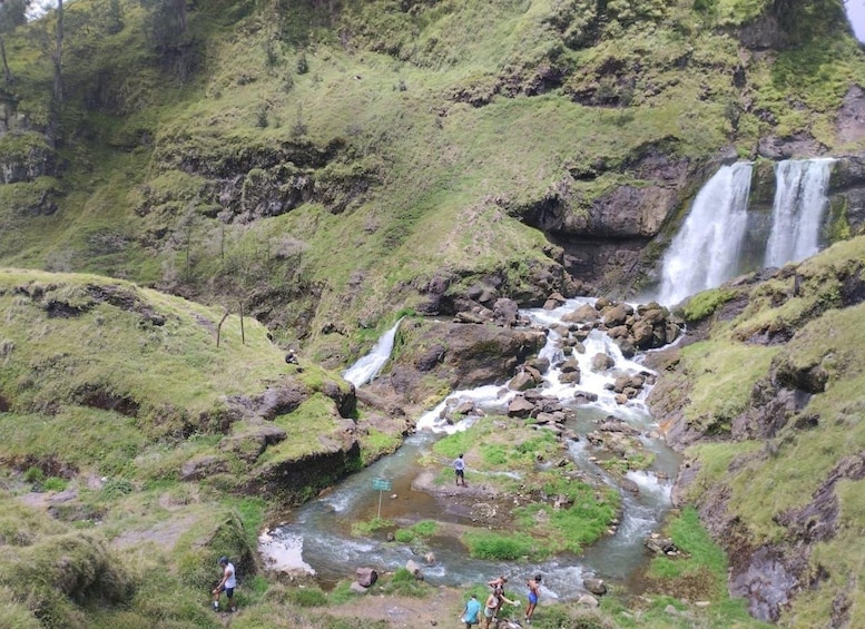 Een waterval stort over rotsen in een rivier, omringd door weelderige groene heuvels. 5