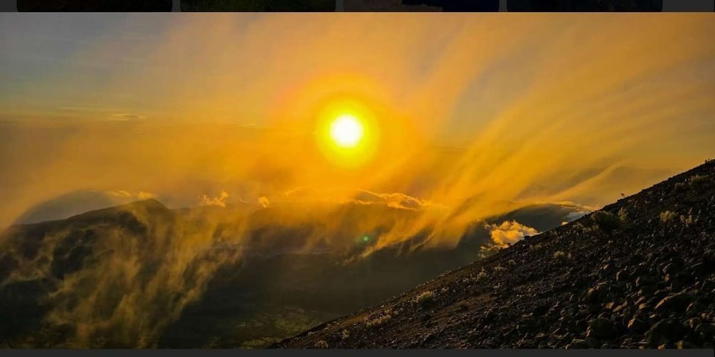 Een zonsondergang boven een bergachtig landschap, waarbij de zon gedeeltelijk verborgen is achter wolken. 4