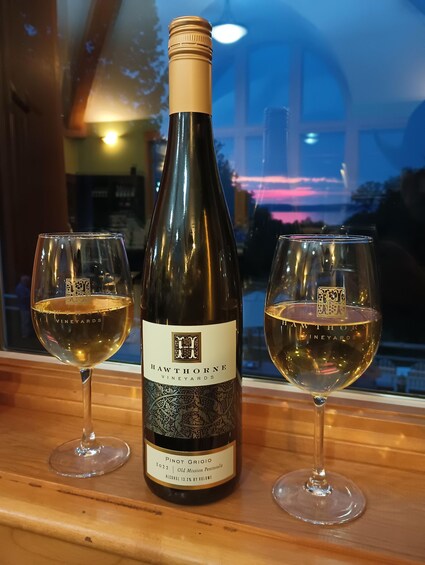 A bottle of Hawthorne Vineyards Pinot Grigio 2022 and two glasses of wine on a wooden surface. 4