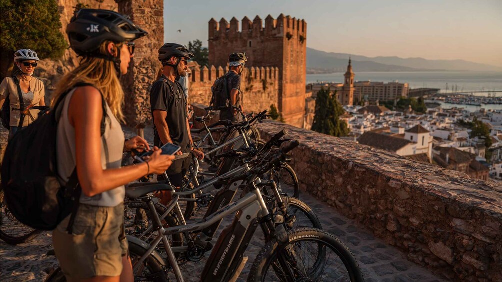 A group of cyclists near a historic stone wall with a castle in the background. 4