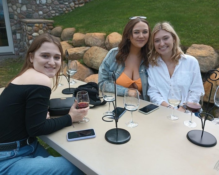 Three people sitting at an outdoor table with wine glasses and a smartphone. 2