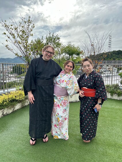 Three people in traditional attire standing on a rooftop with a view of a cityscape and mountains in the background. 3