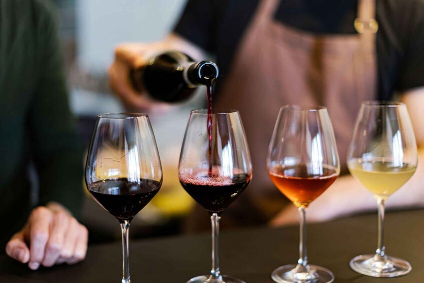 A person pouring wine into four glasses. 5