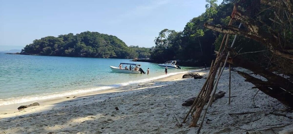 A beach with boats, a sandy shore, and a forested island in the background. 1