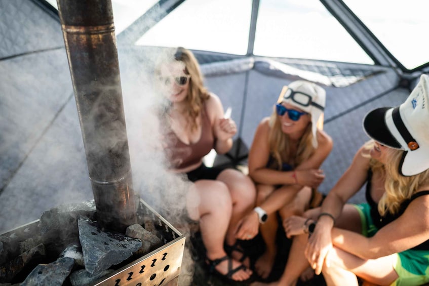A group of people sitting around a portable stove emitting smoke. 1