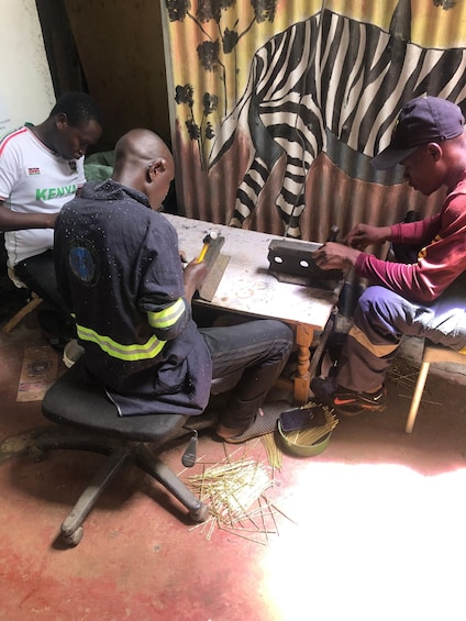 Three men working at a table, one using a hammer and another holding a tool. 5
