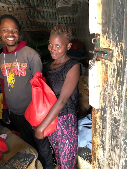 A person holding a red bag in a room with a wooden door and various items in the background. 2