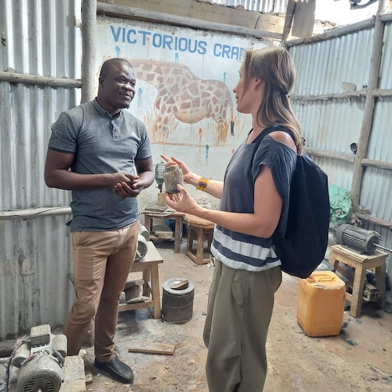 Two people in a workshop with a giraffe mural, tools, and machinery. 1
