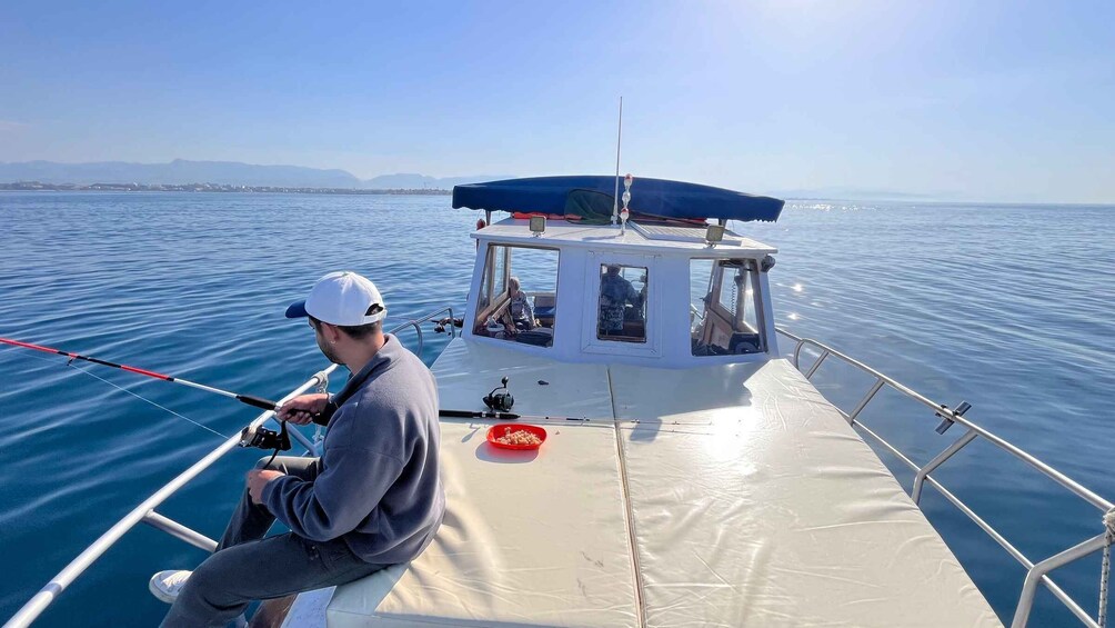 A person fishing on a boat with a clear view of the water and distant mountains. 2