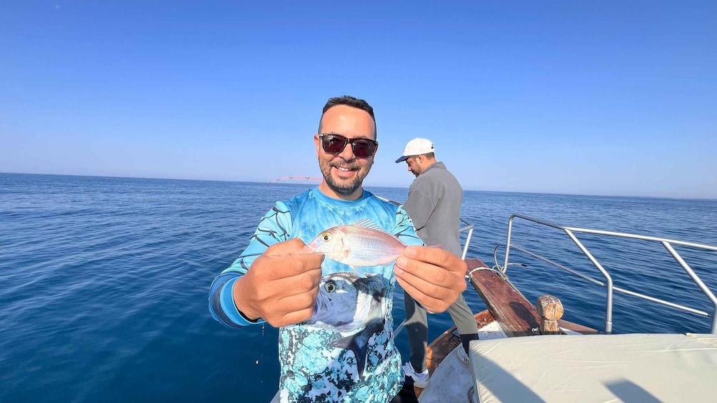 A person holding a fish on a boat with another person in the background. 1