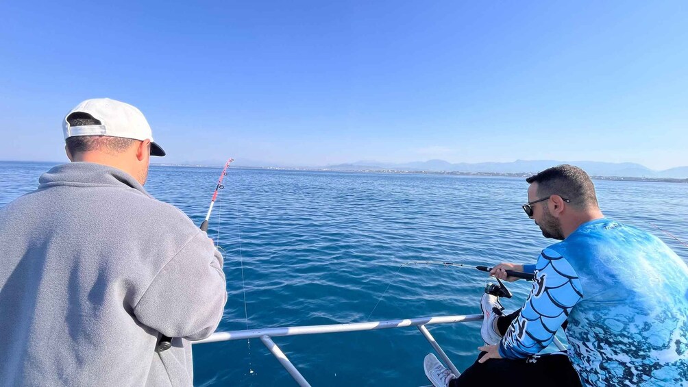 Two people fishing on a boat with a clear view of the sea and distant land. 3