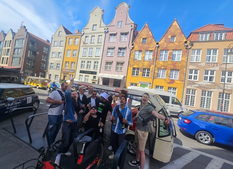 A group of people posing in front of colorful buildings with a parked car and a motorcycle. 4