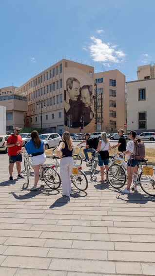 A group of people standing with bicycles in front of a building with a large mural. 2
