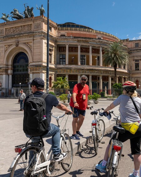 Three people on bicycles in front of a historic building with columns and statues. 5