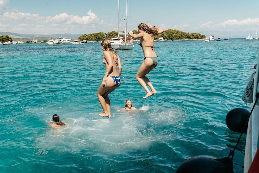 Two people jumping into the water from a boat, with a clear blue sea and boats in the background. 4