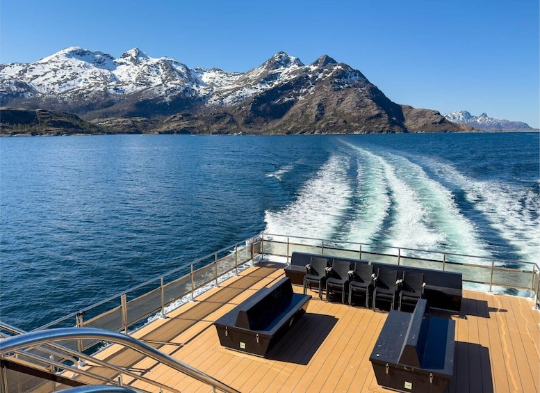 A boat deck with outdoor seating and a view of snow-capped mountains across a body of water. 3