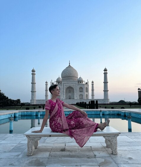A person in a pink saree sitting on a bench with the Taj Mahal in the background. 3