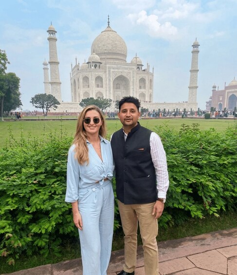 Two people standing in front of the Taj Mahal with its domes and minarets visible in the background. 5