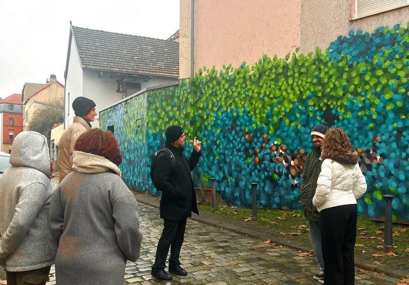 A group of people standing in front of a wall covered with blue and green graffiti. 1