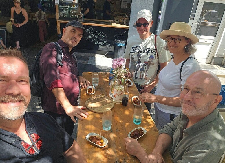A group of people sitting at an outdoor wooden table with drinks and food. 5