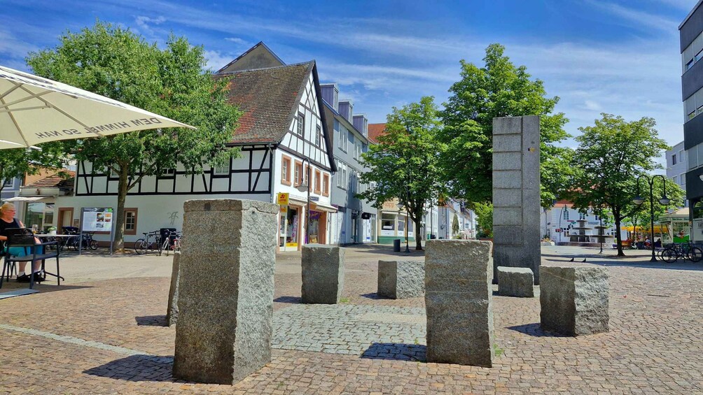 A cobblestone square with stone pillars, traditional half-timbered buildings, and a café with outdoor seating. 5