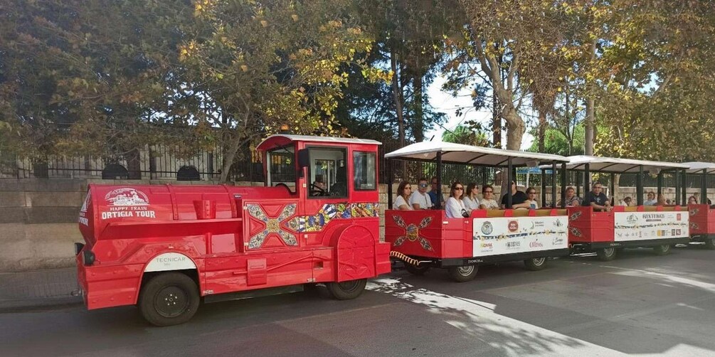 A red trolley with passengers, surrounded by trees and a stone wall. 1